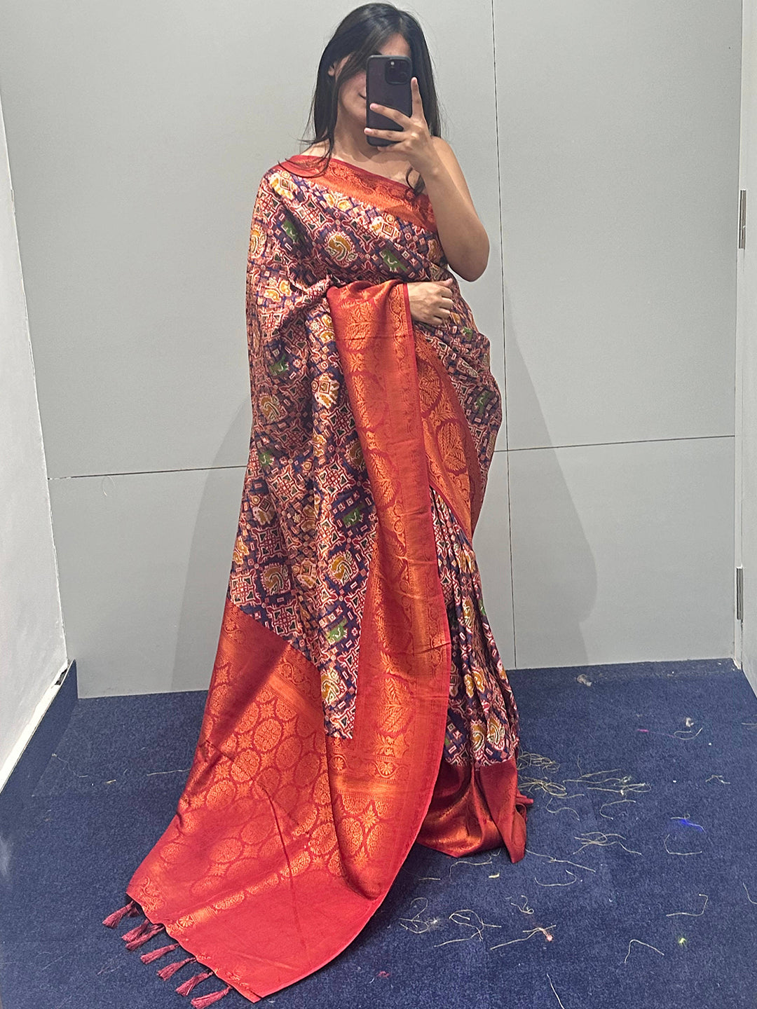 Woman taking a mirror selfie in red Patola saree with intricate design.