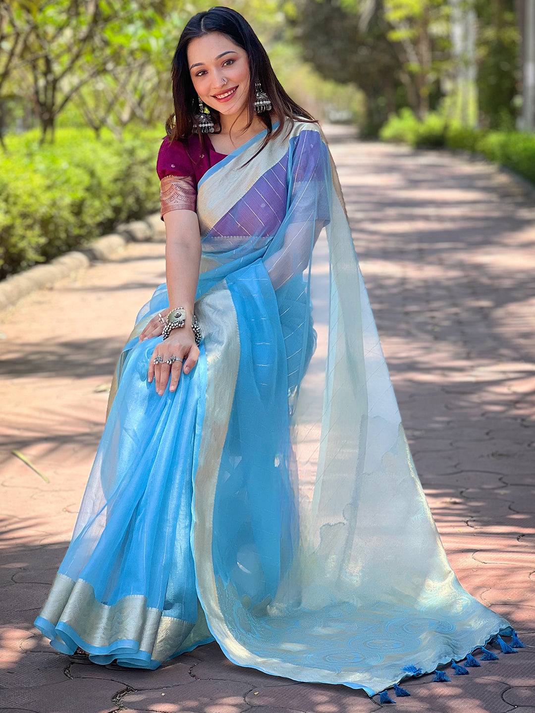 Model seated in blue organza saree with gold zari weaving