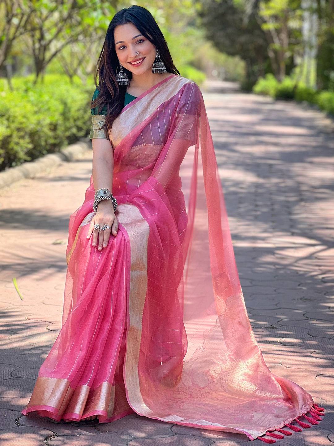 Model seated in dark pink organza saree with gold zari border.