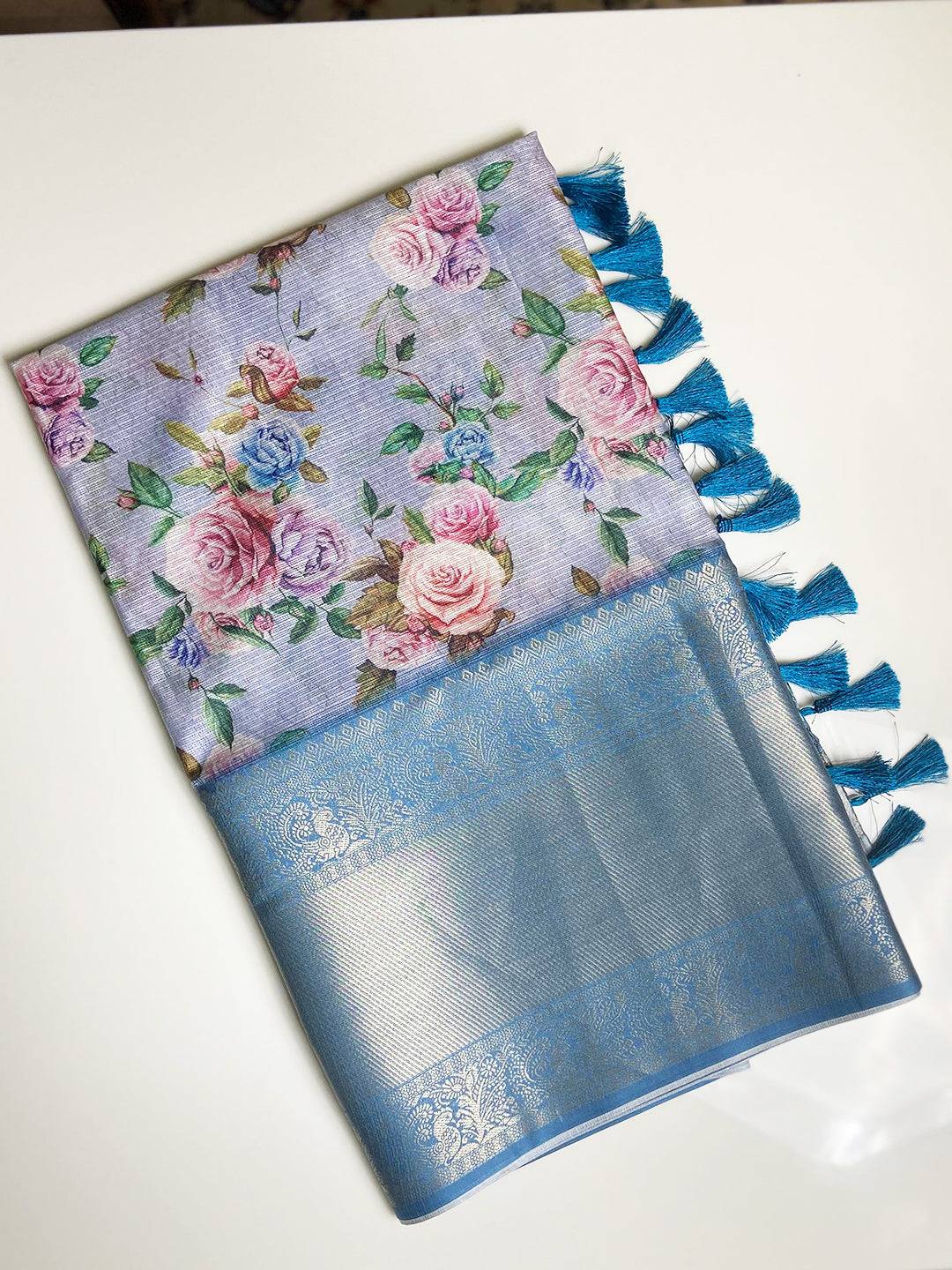 Folded lavender saree with floral design and blue tassels