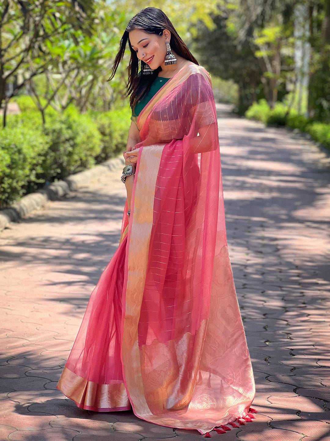 Elegant dark pink organza saree with gold zari border, outdoor setting.