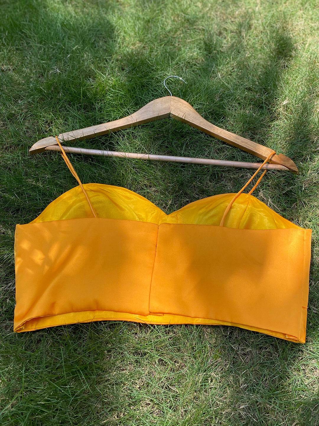 Back view of yellow satin blouse on hanger on grass