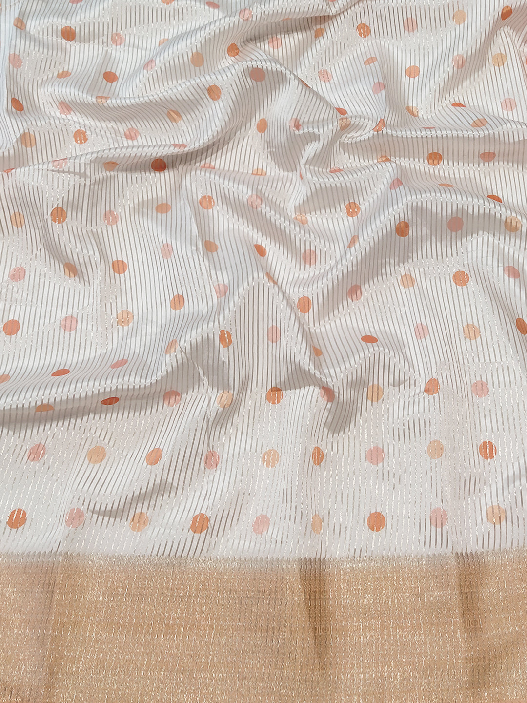 Close-up of organza saree fabric with polka dots and golden border.